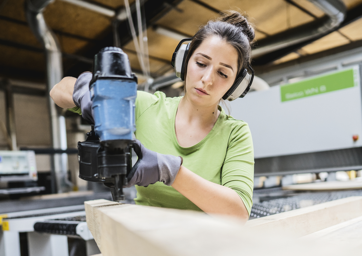 Handwerkerin arbeitet mit Nagelpistole an einem Holzstück